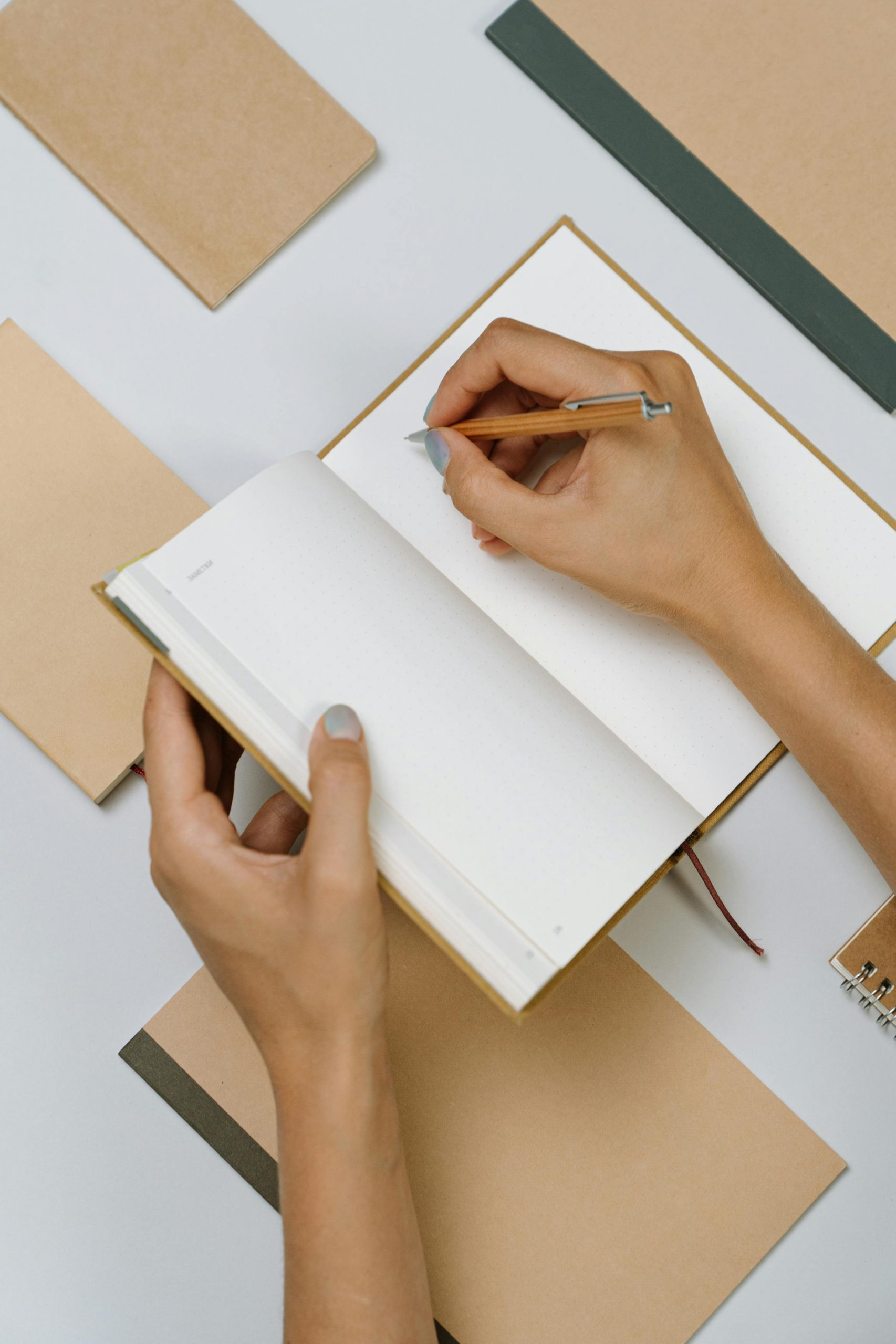 Top view of hands writing in an open notepad surrounded by stationery items.