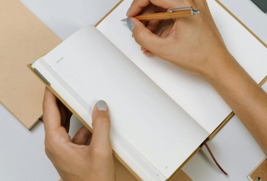 Top view of hands writing in an open notepad surrounded by stationery items.